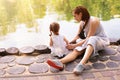 Little Caucasian girl sitting next to her mother on the shore of an artificial lake in the park. Mother with daughter on a walk on Royalty Free Stock Photo