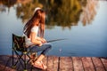 Little Caucasian girl sitting on a wooden pier with fishing rod Royalty Free Stock Photo