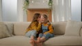 Little Caucasian girls kids children sisters friends daughters on couch living room whisper secret in ear tell amazing Royalty Free Stock Photo