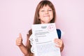 Little caucasian kid girl with long hair showing a passed exam from primary school smiling happy and positive, thumb up doing Royalty Free Stock Photo