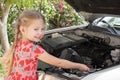Little caucasian smiling girl fixing the engine of a car with an open car hood Royalty Free Stock Photo