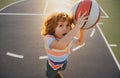 Little caucasian sports kid playing basketball holding ball with funy face.