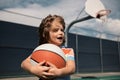 Little caucasian sports kid playing basketball holding ball with happy face. Active kids lifestyle. Portrait of sporty