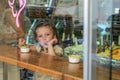 ROMA, ITALY - AUGUST 2018: Little charming baby girl eating ice cream in a cafe, view through the window