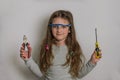 Little charming baby girl in safety glasses with screwdriver and pliers tools on a light background