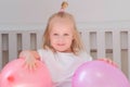 Little charming blond girl sitting on bed in her room with pink balloons and smiling. Portrait. Royalty Free Stock Photo