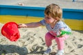 Little charming girl baby playing on the playground in the sandbox sand mound in the bucket with a shovel and rake Royalty Free Stock Photo