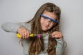 Little charming girl child in safety glasses turns a screwdriver screw