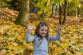 Little charming girl child throws up fallen yellow maple leaves in autumn park