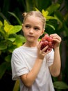 Little charming girl holding bunch of red grapes near her face. Selected focus. Green tropical leaves background. Organic fruit Royalty Free Stock Photo