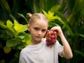 Little charming girl holding bunch of red grapes near her face. Selected focus. Green tropical leaves background. Organic fruit Royalty Free Stock Photo