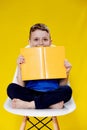 Little cheerful blond green-eyed boy 5-6 years old in a stylish blue T-shirt holding book and reading on yellow wall Royalty Free Stock Photo