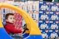 a little cheerful boy in red sweater in a children& x27;s car in a shopping center on a background of diapers Royalty Free Stock Photo