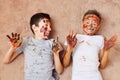 Little cheerful boys with paint on face and hands lying on floor and laughing Royalty Free Stock Photo