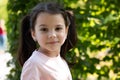 Little cheerful girl with ponytails smiling looks ahead against a background of green blurred foliage Royalty Free Stock Photo