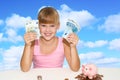 Little lovely girl sitting on the desk with coins and pink piggy bank and holding in hands european currency over blue sky