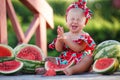 Little cheerful girl sitting outdoors in a park near a pile of ripe, red watermelons Royalty Free Stock Photo