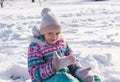 Little cheerful girl, 7-8 years old, in bright winter overalls, sits on the snow