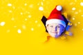 Little cheerful Santa in hat smiles, getting out of the ragged yellow background lit by neon light Royalty Free Stock Photo