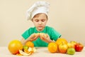 Little chef peeling fresh orange at table with fruits Royalty Free Stock Photo