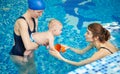 Infant accustoming to water at first lesson in pool. Women entertain and amuse baby to not afraid swimming. Side view Royalty Free Stock Photo