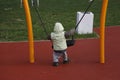 Little child in autumn jackets swinging in a swing his back turned Royalty Free Stock Photo