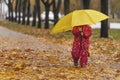 Little child in autumn park. Child hid behind large yellow umbrella and walks on the fallen leaves Royalty Free Stock Photo