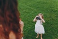 Little child baby girl in light dress take picture of mom on retro vintage photo camera on green grass in park. Mother Royalty Free Stock Photo