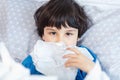 Little child boy blow his nose. Sick child with napkin in bed. Allergic kid, flu season. Kid with cold rhinitis, get cold