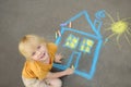 Little child boy is drawing house and sun painted with colored chalk on asphalt of sidewalk. Kids creative picture on gray Royalty Free Stock Photo