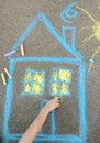 Little child boy is drawing house and sun painted with colored chalk on asphalt of sidewalk. Kids creative picture on gray Royalty Free Stock Photo