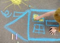 Little child boy is drawing house and sun painted with colored chalk on asphalt of sidewalk. Kids creative picture on gray Royalty Free Stock Photo