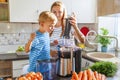 Little child boy with mother makes fresh carrot juice with juicer in kitchen Royalty Free Stock Photo