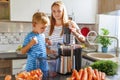 Little child boy with mother makes fresh carrot juice with juicer in kitchen Royalty Free Stock Photo