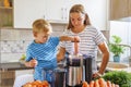 Little child boy with mother makes fresh carrot juice with juicer in kitchen Royalty Free Stock Photo