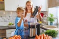 Little child boy with mother makes fresh carrot juice with juicer in kitchen Royalty Free Stock Photo