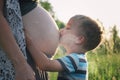 Little child boy older brother kissing pregnant mother belly. Pregnancy woman outdoor. Authentic family moments of expecting baby Royalty Free Stock Photo