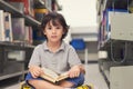 Little child boy reading a book in library.