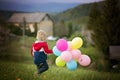 Little child, cute boy on a spring cold windy rainy day, holding colorful balloons in a field, running Royalty Free Stock Photo