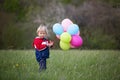 Little child, cute boy on a spring cold windy rainy day, holding colorful balloons in a field, running Royalty Free Stock Photo