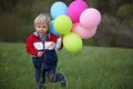 Little child, cute boy on a spring cold windy rainy day, holding colorful balloons in a field, running Royalty Free Stock Photo