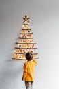 Little child decorating handmade craft Christmas tree made from sticks and natural materials hanging on wall.