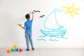 Little child drawing boat at sea on white wall