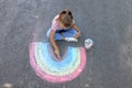 Little child drawing rainbow with colorful chalk on asphalt, above view Royalty Free Stock Photo