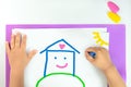 little child draws a house with wax crayons on white paper, concept of a happy childhood and family, home sweet home Royalty Free Stock Photo