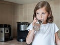 Little child is drinking clean water at home, close up. Caucasian cute girl with long hair is holding a water glass in her hand Royalty Free Stock Photo