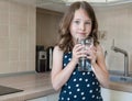 Little child is drinking clean water at home, close up. Caucasian cute girl with long hair is holding a water glass in her hands Royalty Free Stock Photo