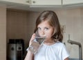 Little child is drinking clean water at home, close up. Caucasian cute girl with long hair is holding a water glass in her hands Royalty Free Stock Photo