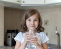 Little child is drinking clean water at home, close up. Caucasian cute girl with long hair is holding a water glass Royalty Free Stock Photo