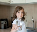 Little child is drinking clean water at home, close up. Caucasian cute girl with long hair is holding a water glass in her hand Royalty Free Stock Photo